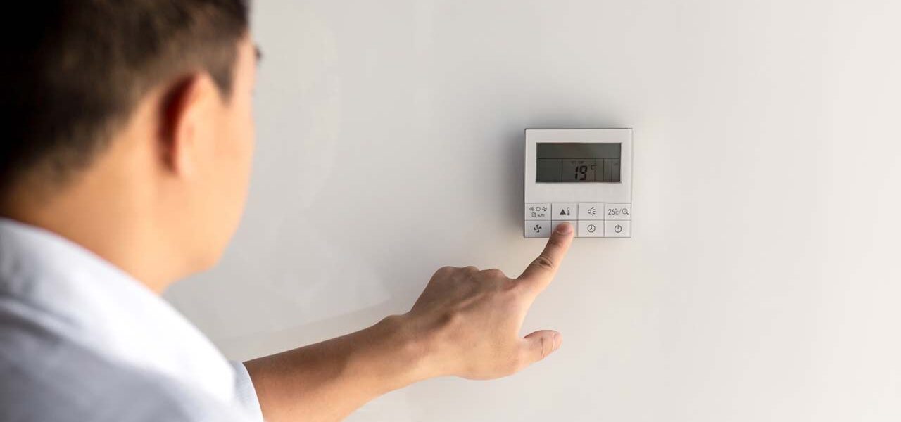 the finger of a man presses the buttons of the thermostat