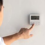 the finger of a man presses the buttons of the thermostat