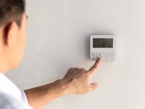 the finger of a man presses the buttons of the thermostat